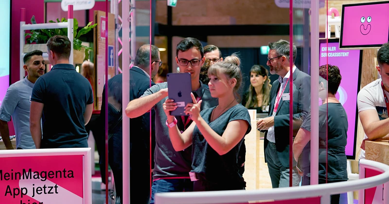 Weitwinkelaufnahme des Telekom‑Stands mit Besuchern an den interaktiven Stationen, idealerweise AR‑Gate im Vordergrund und Menschen in Aktion als lebendige Szene.