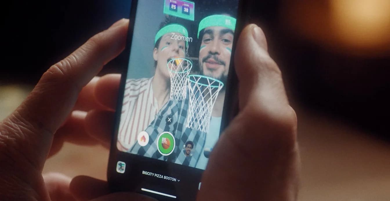 Placeholder: Person nutzt AR Facefilter, hält geöffnete BIG CITY Pizzabox, auf dem Display sind City‑Grafiken und Game‑Elemente sichtbar.